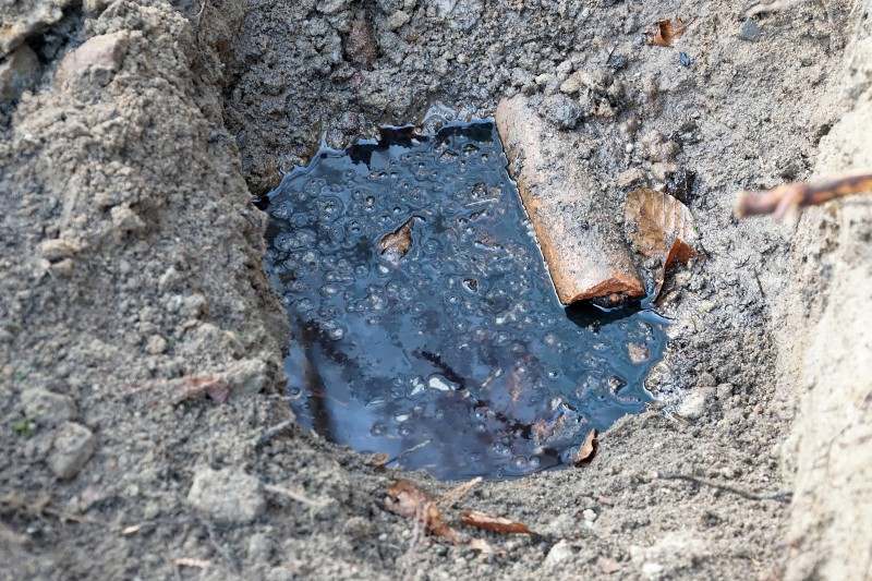 Contaminated liquid pooled in the soil near a broken pipe