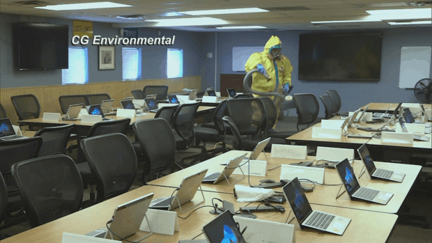 Hazmat worker disinfecting an office workspace with laptops