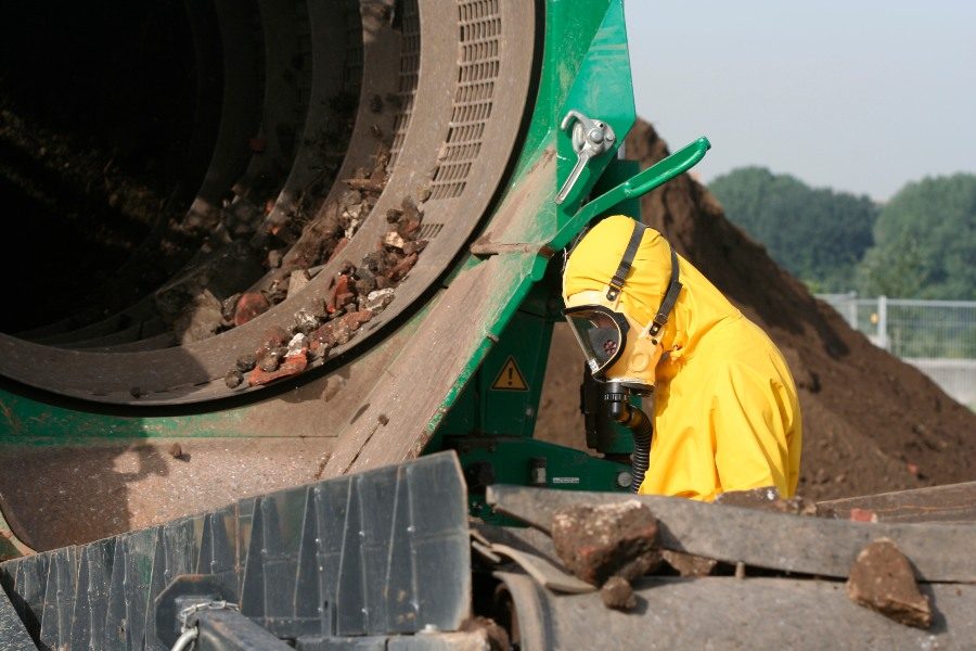 A worker in a hazmat suit is inspecting industrial machinery at a cleanup site
